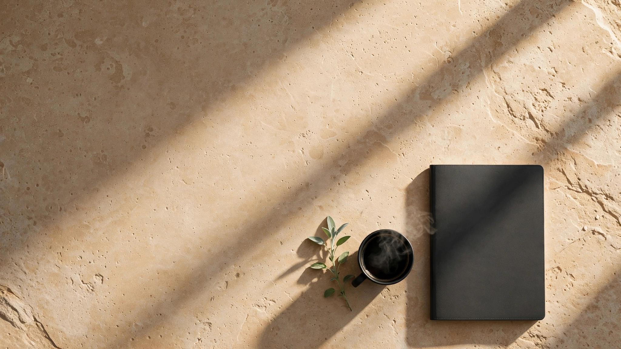 Espacio de trabajo minimalista con cuaderno, café y hoja de salvia sobre piedra arena