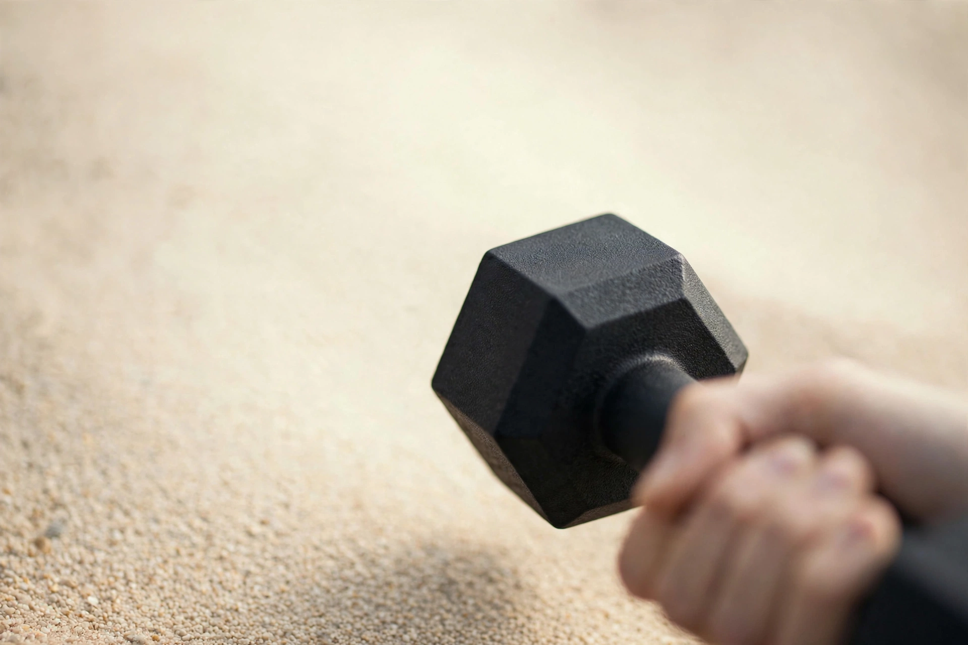 Mano sujetando una pesa hexagonal negra sobre arena